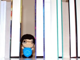 Small crocheted person standing in a gap between several standing books.